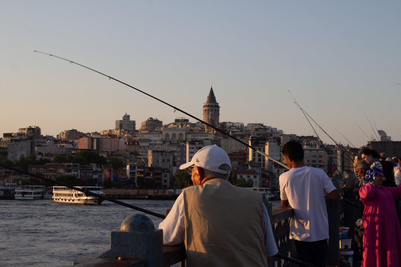 People fishing at sunset on Galata Bridge with a view of the historic Galata Tower, Istanbul.